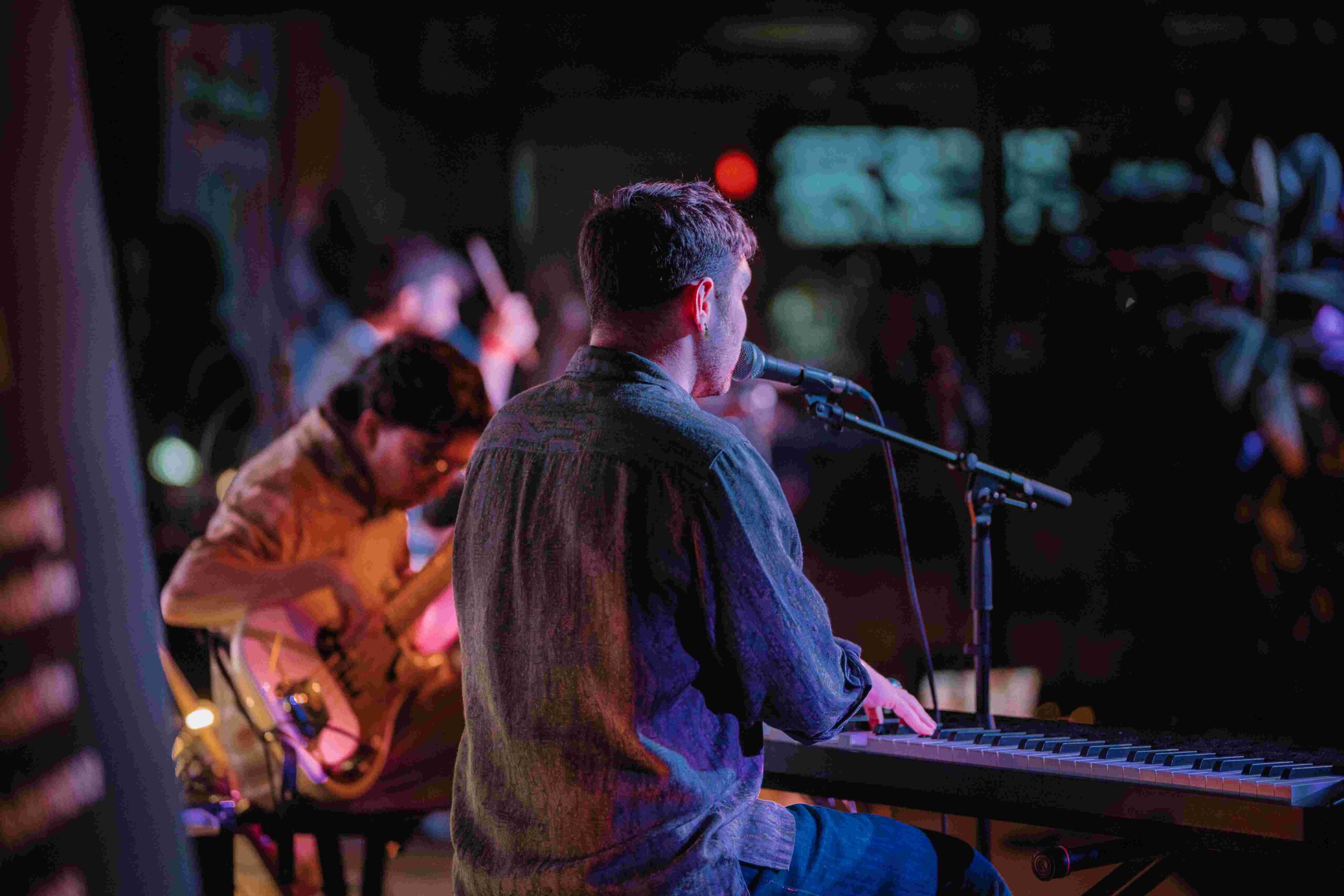 Person playing piano in the foreground with person playing guitar in the background.