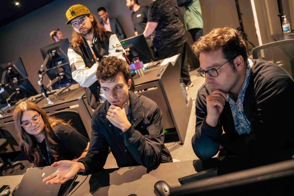 Three people sat at a desk looking at something. One person stood up behind them.