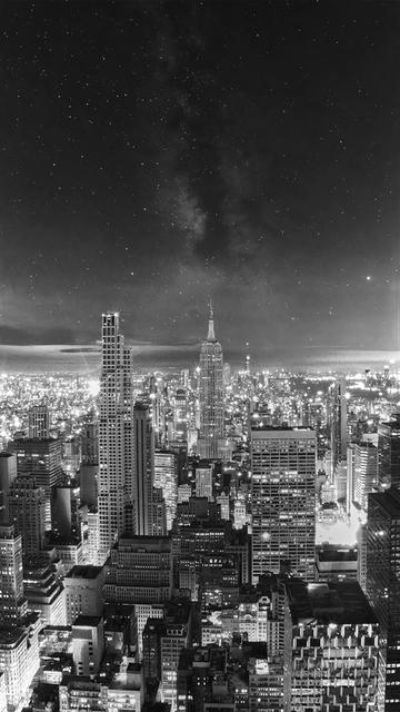 A black and white view of the Manhattan skyline merges into a night sky with stars and a visible, though faint, Milky Way.
