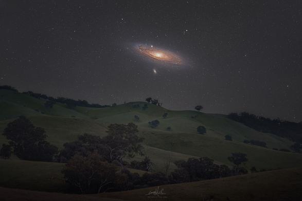 The Andromeda galaxy above rolling hills.