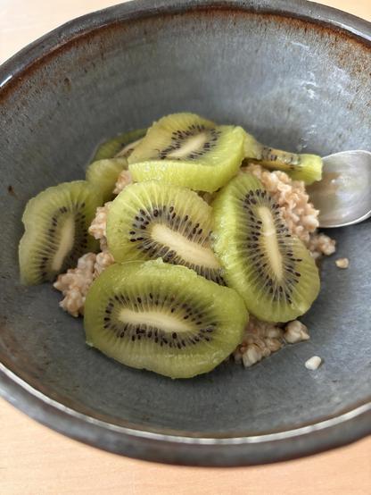 A bowl of oatmeal with sliced kiwi on it. The kiwi looks kinda gross, like a swarm of alien bugs. 🐛