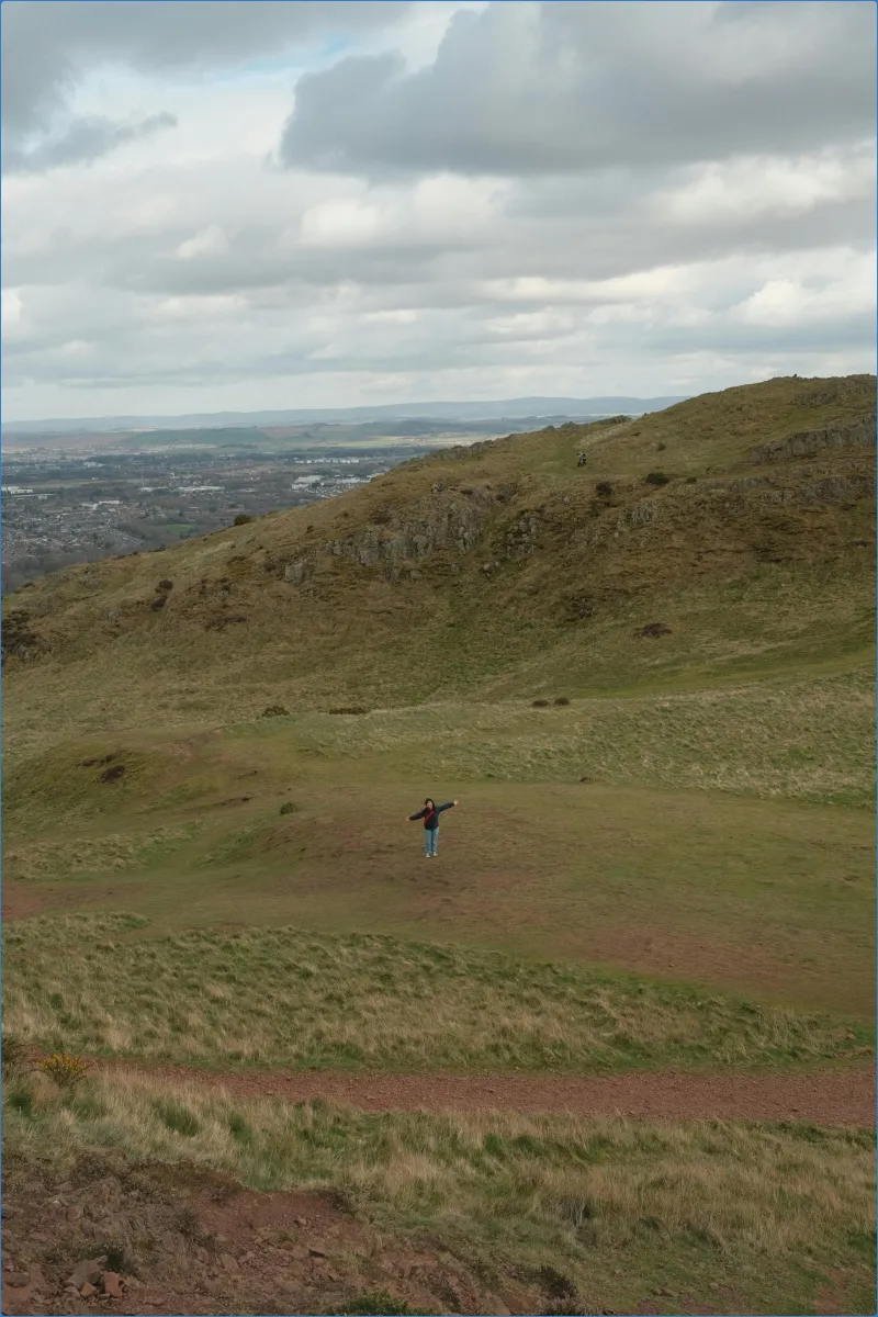 Person standing on a grassy hill with arms outstretched.