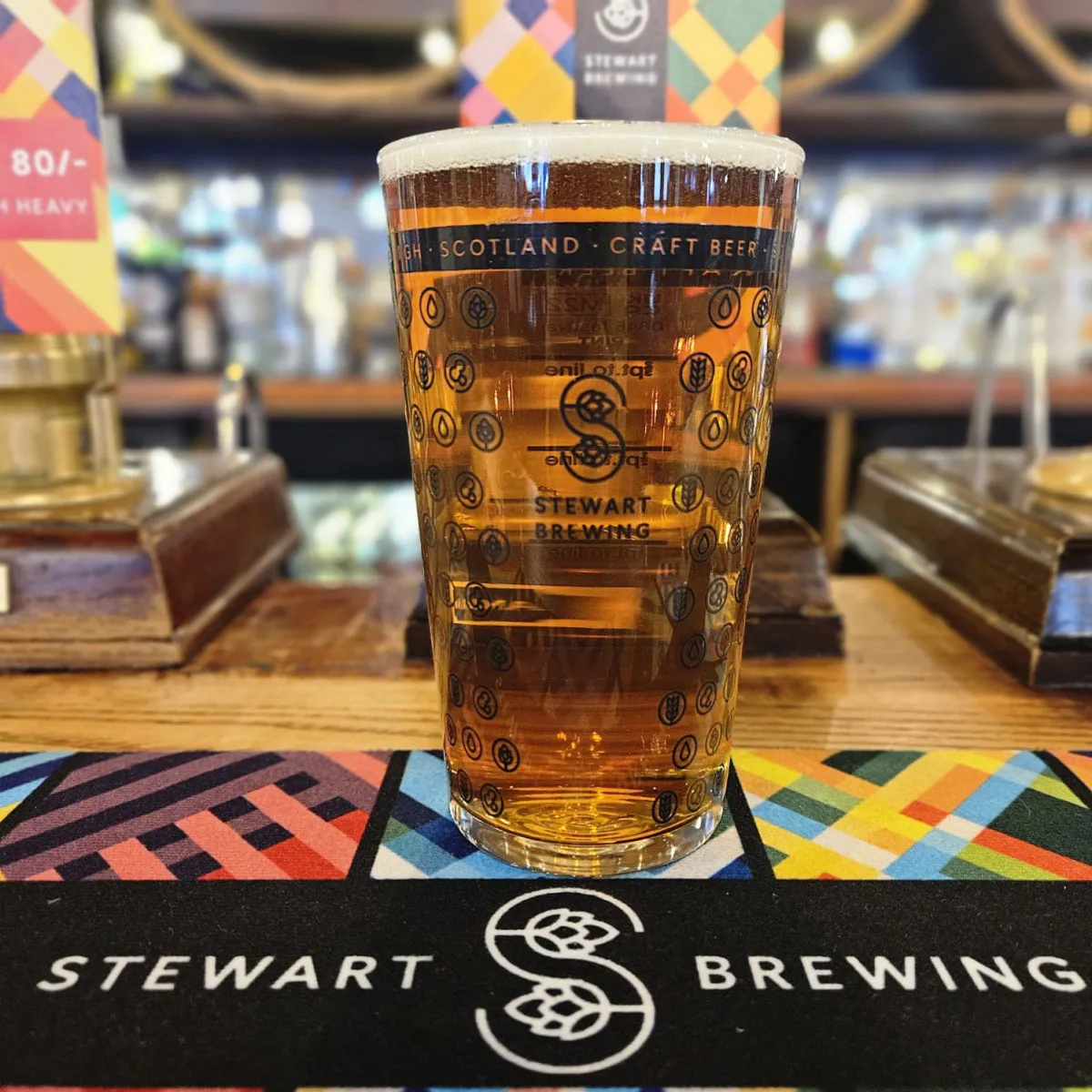 Pint glass of Stewart Brewing beer on a bar counter.