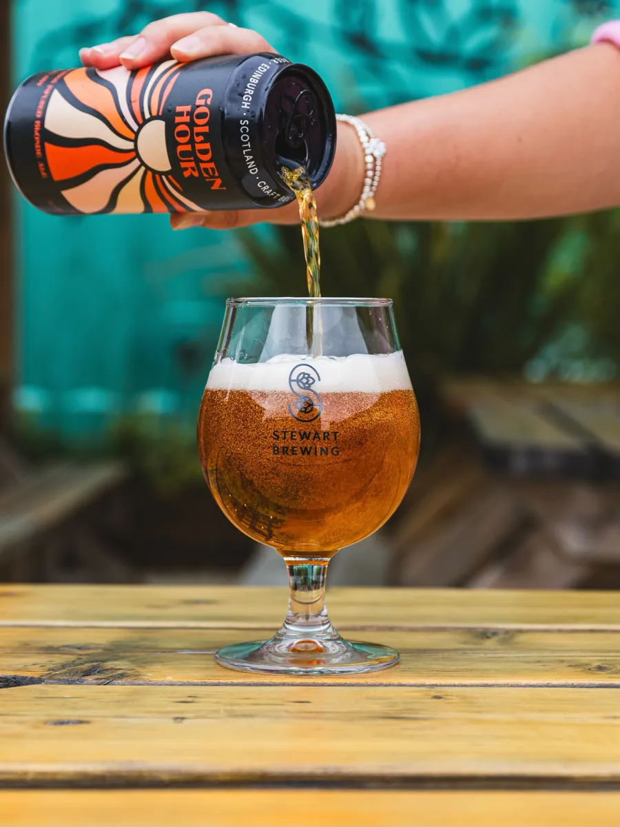 Pouring beer from can into a glass on a table.