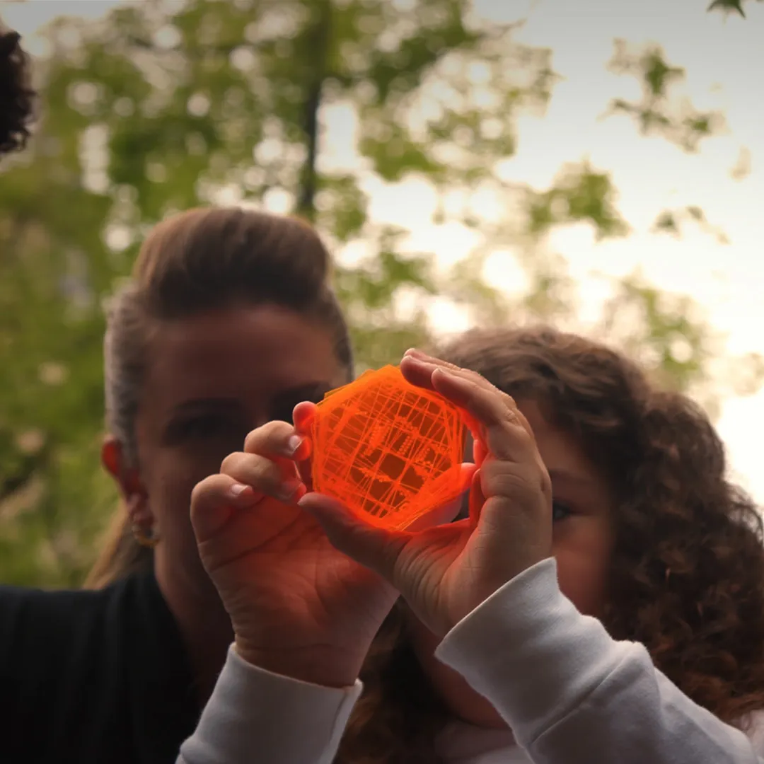 Person holding an orange geometric object outdoors.