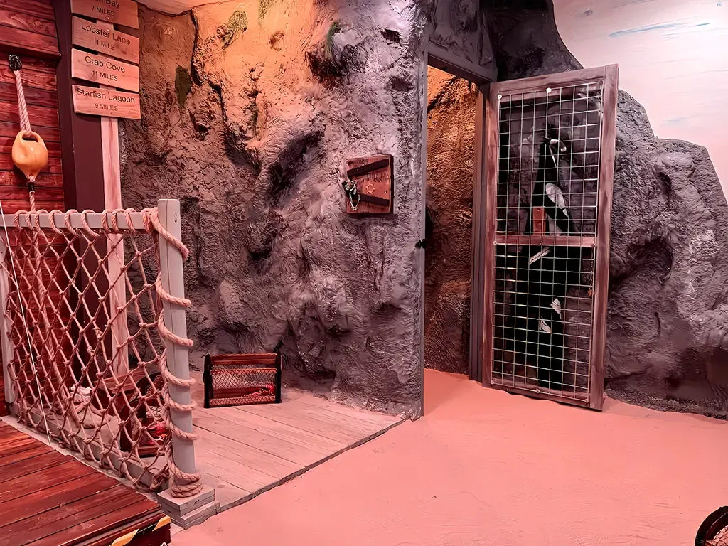 Indoor cave-like setting with a rope bridge and bird enclosure.