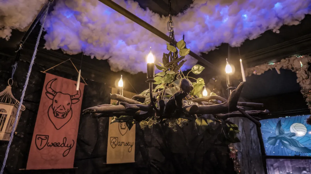 Rustic chandelier with candles and banners in a themed room.