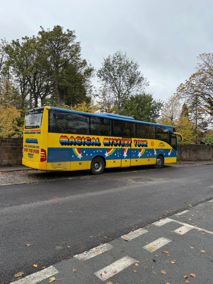 Yellow bus with 'Magical Mystery Tour' text parked on roadside.