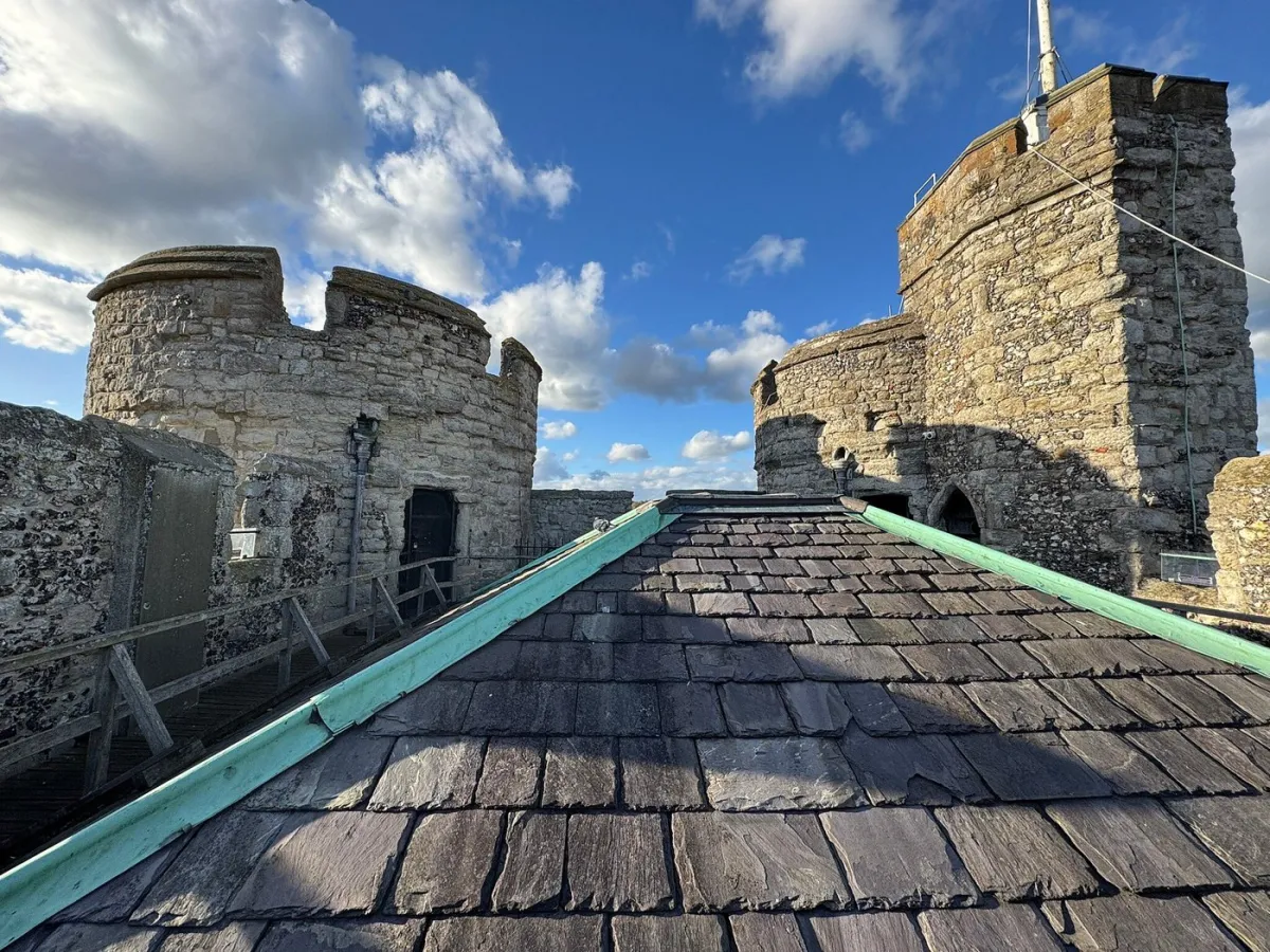 Stone towers and slate roof under a blue sky with clouds.