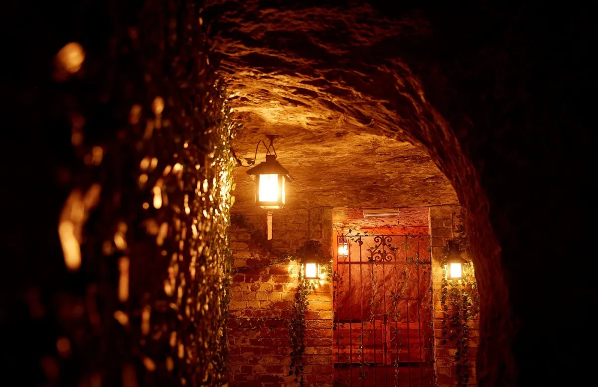Dimly lit brick tunnel with lanterns and iron gate