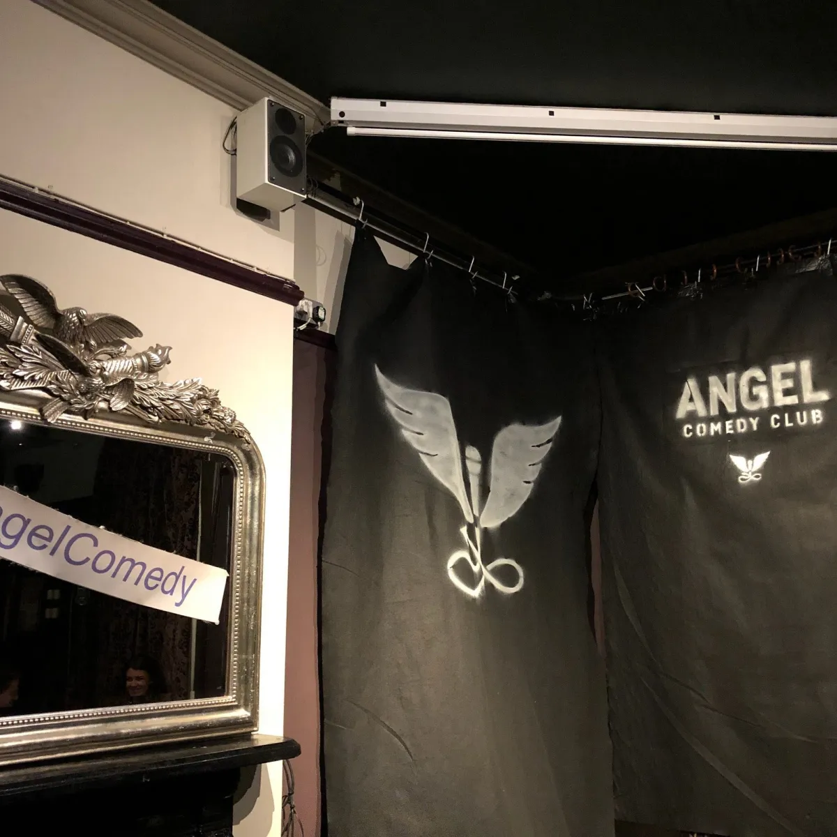 Stage with Angel Comedy Club backdrop and mirror.
