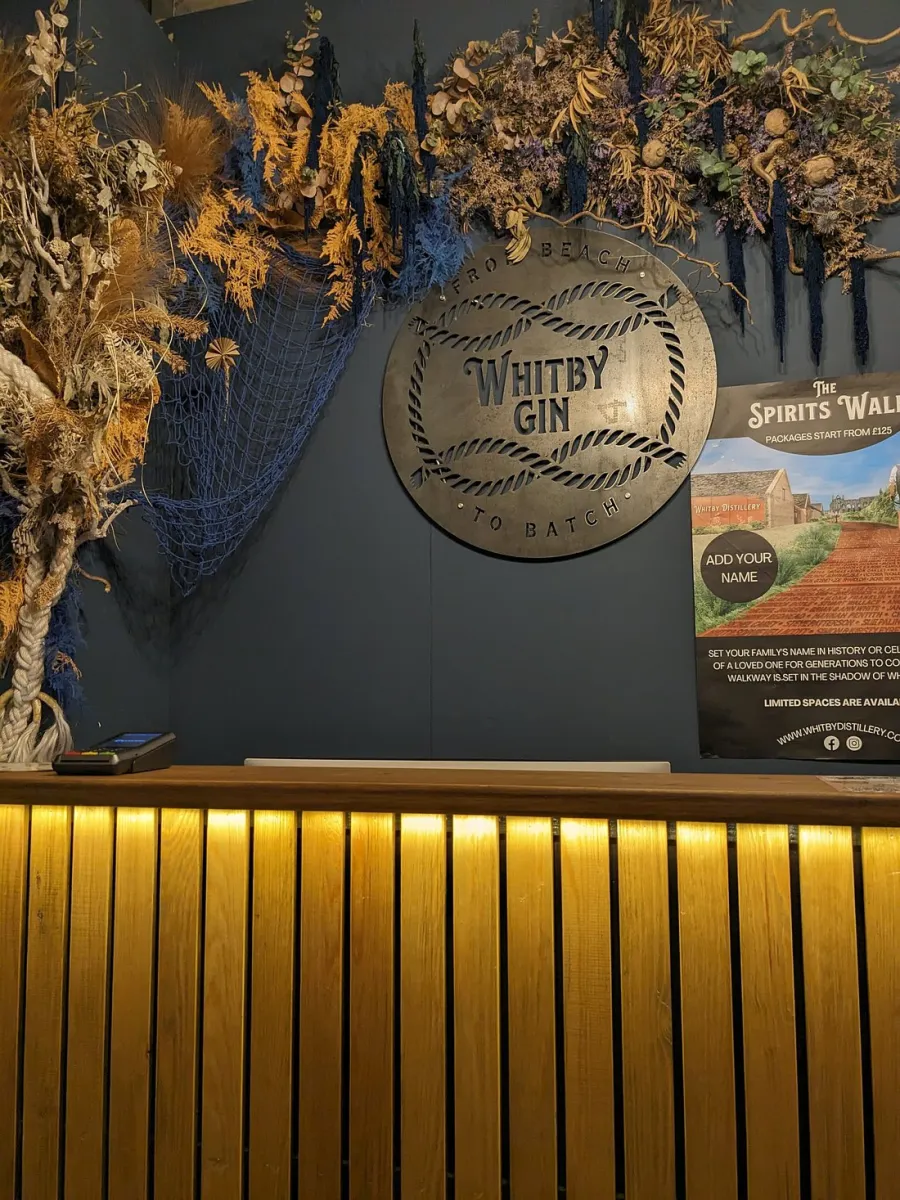 Whitby Gin sign above a wooden counter with dried flowers.