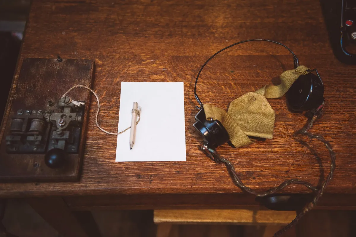 Vintage telegraph key and headphones on a wooden table.