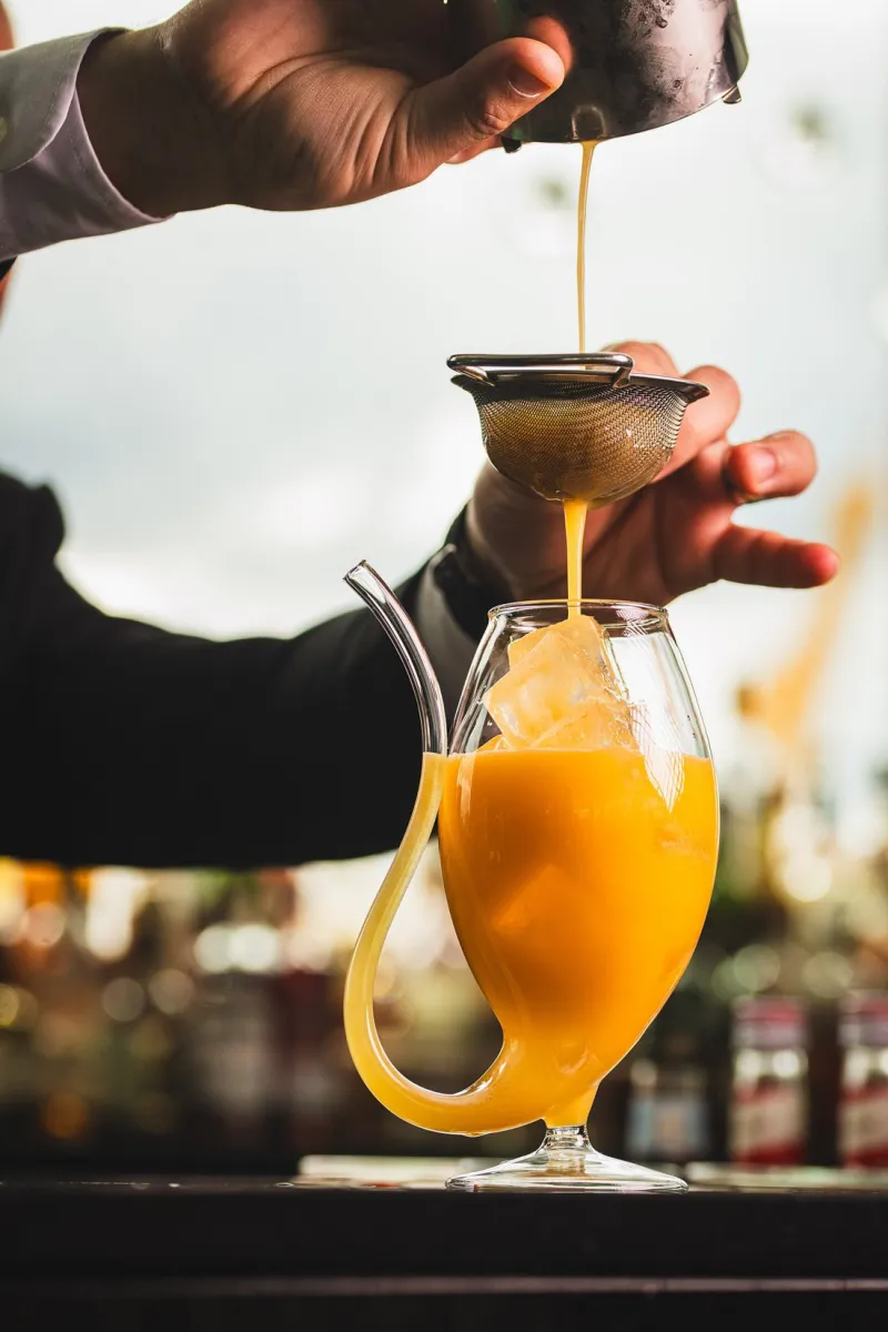 Bartender straining orange cocktail into a glass