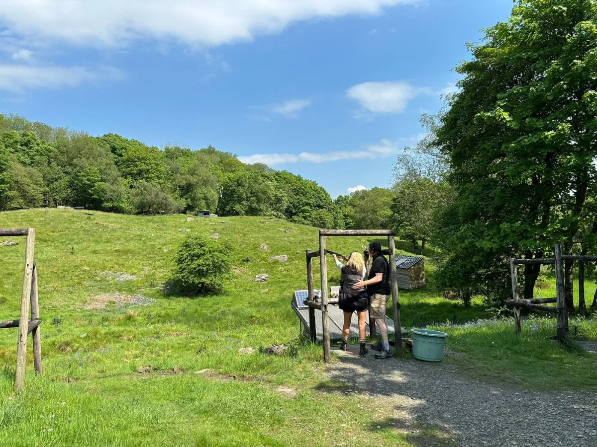 Two people at an outdoor archery range with green landscape.