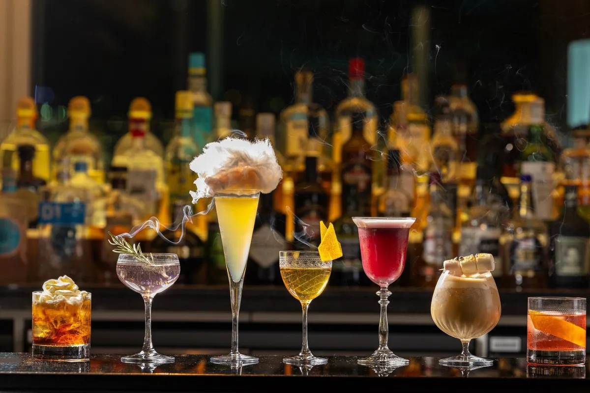 Assorted cocktails on a bar counter with bottles in the background