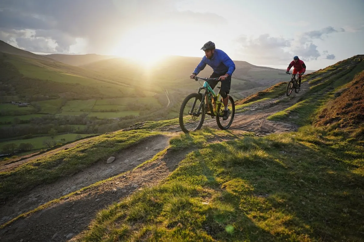 Two cyclists riding on a mountain trail at sunset.