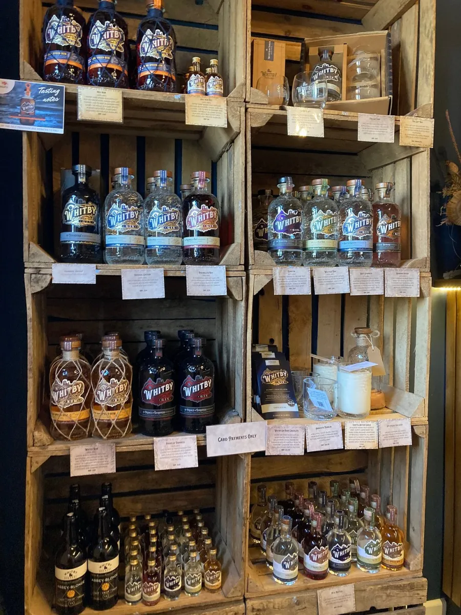 Display of various Whitby gin bottles on wooden shelves.
