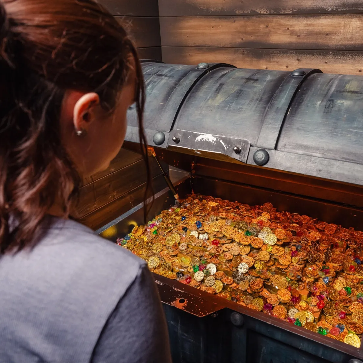 Person looking at an open treasure chest filled with coins.