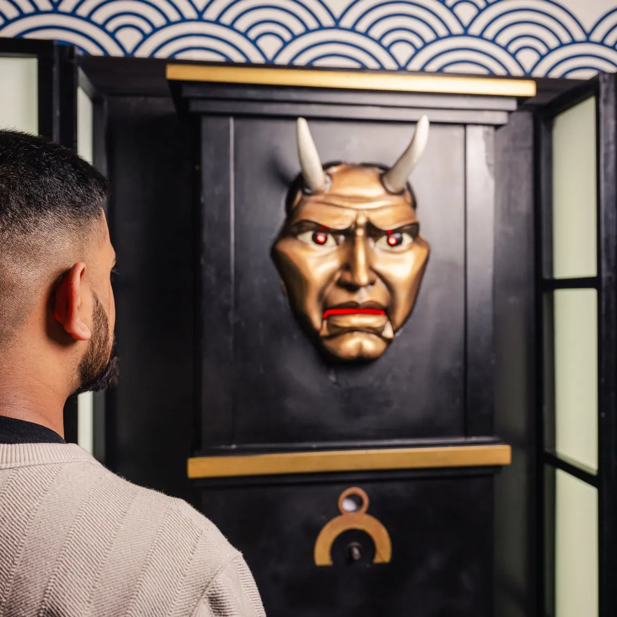 Man looking at a decorative mask with horns on a wall.