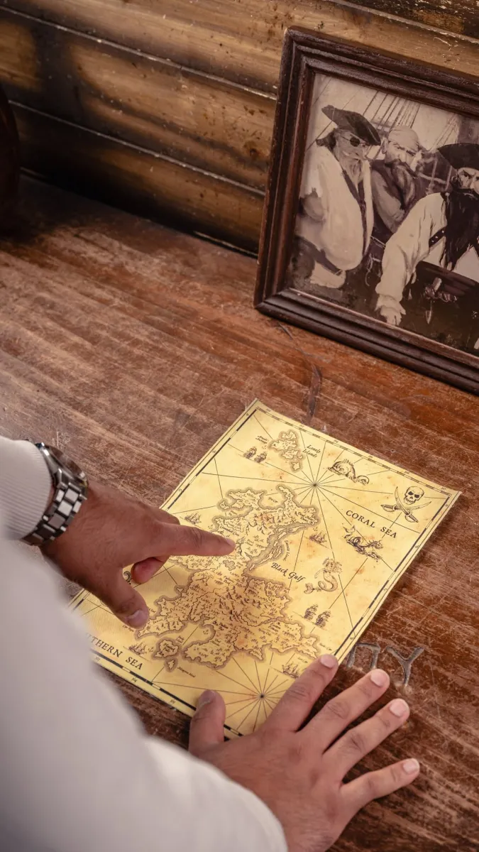 Person pointing at a vintage treasure map on a wooden table.