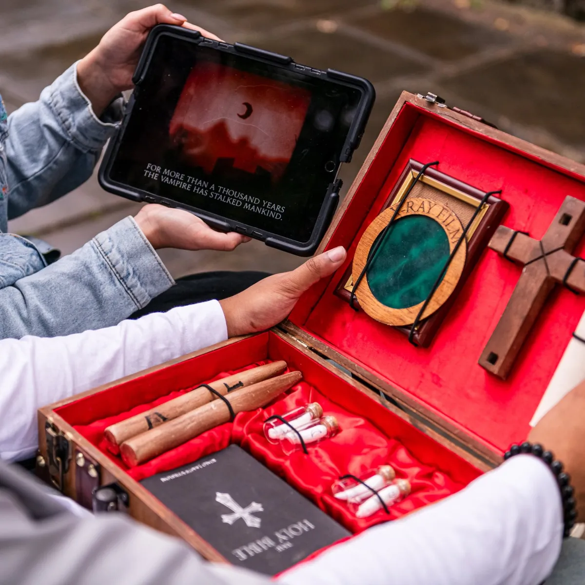 Person holding a tablet with vampire text and a box with a cross.