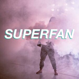 A figure in a silver boiler suit stands surrounded by a cloud of pink smoke, obscuring their face and upper body. SUPERFAN is written in bold white and green text over them.