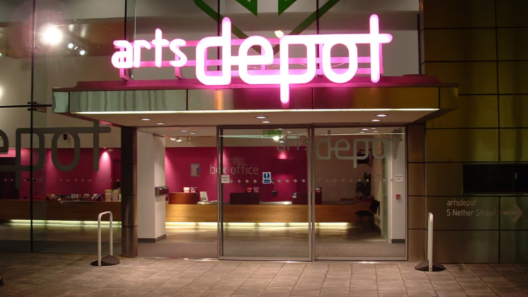 Illuminated artsdepot sign above the main entrance, with glass doors opening into the foyer and box office.