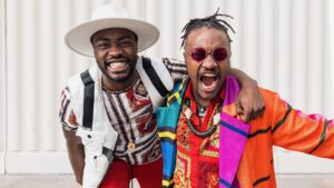 Image of Anthony and Kel Matsena, two black men in their twenties, wearing colourful, African patterned clothes and grinning like maniacs